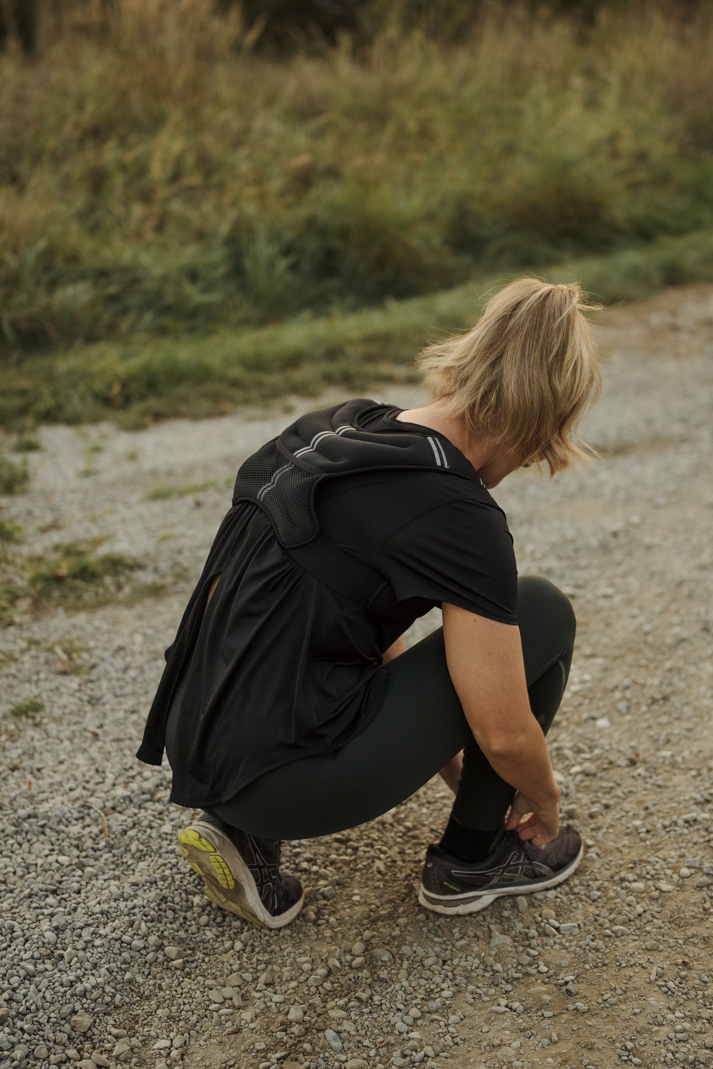 Rear view of a lady doing up her shoe lace while wearing a black neoprene VestFit NZ weighted vest