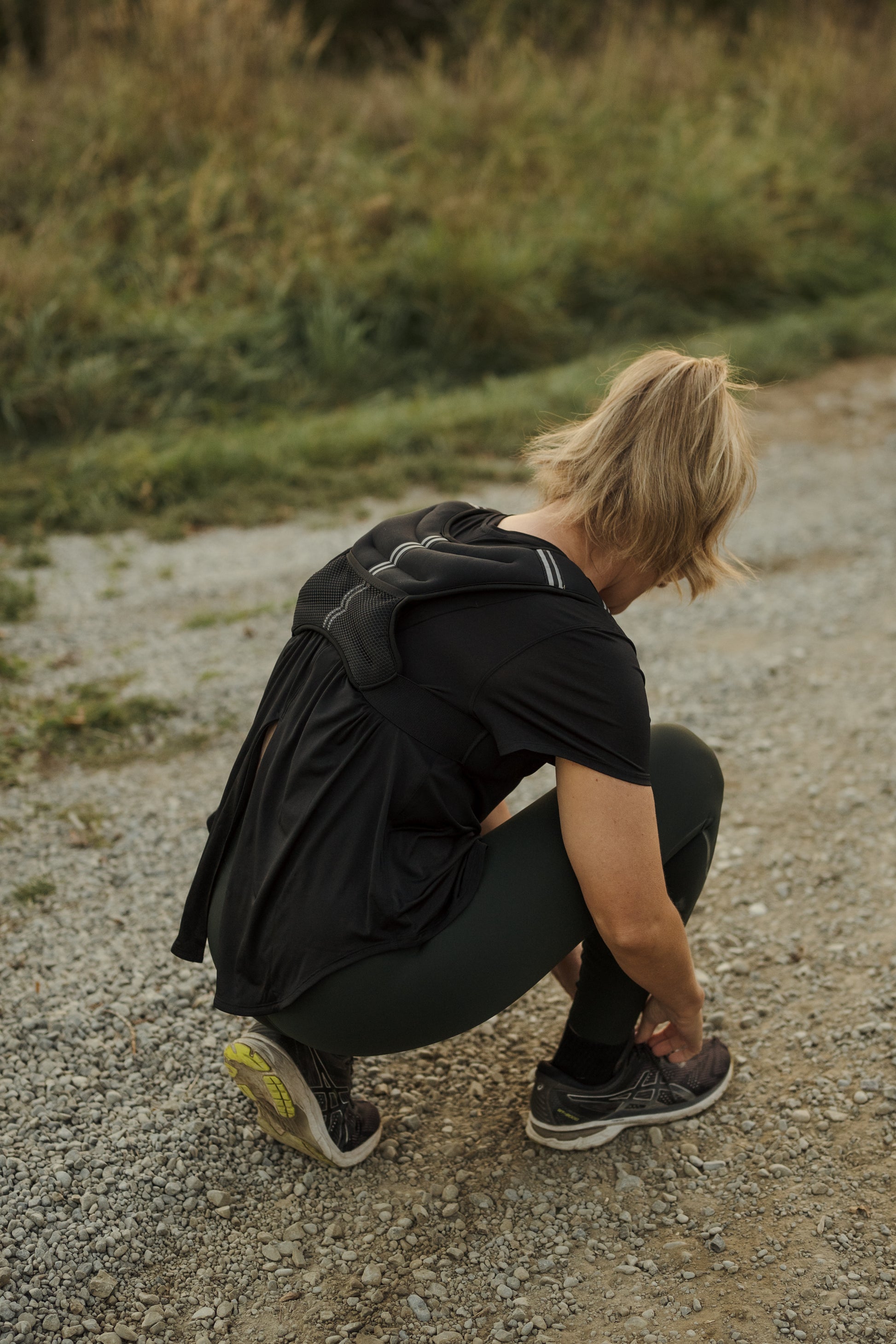 Rear view of a lady doing up her shoe lace while wearing a black neoprene VestFit NZ weighted vest