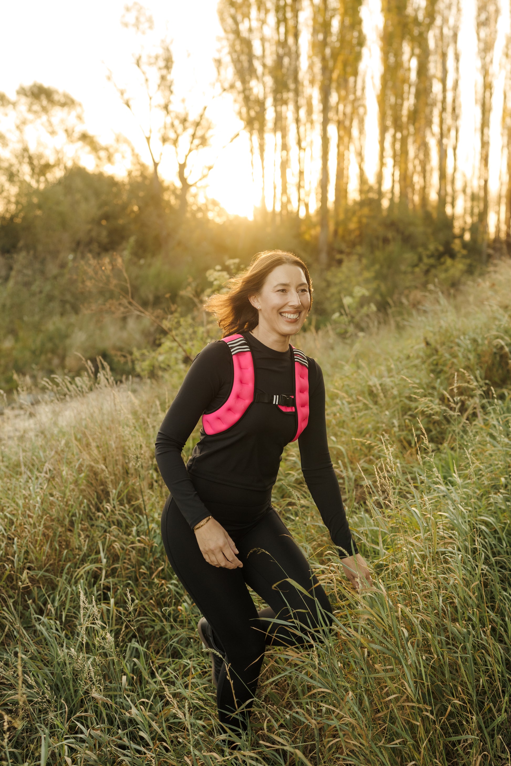 A lady exercising in the VestFit NZ pink weighted neoprene vest through forest grasses