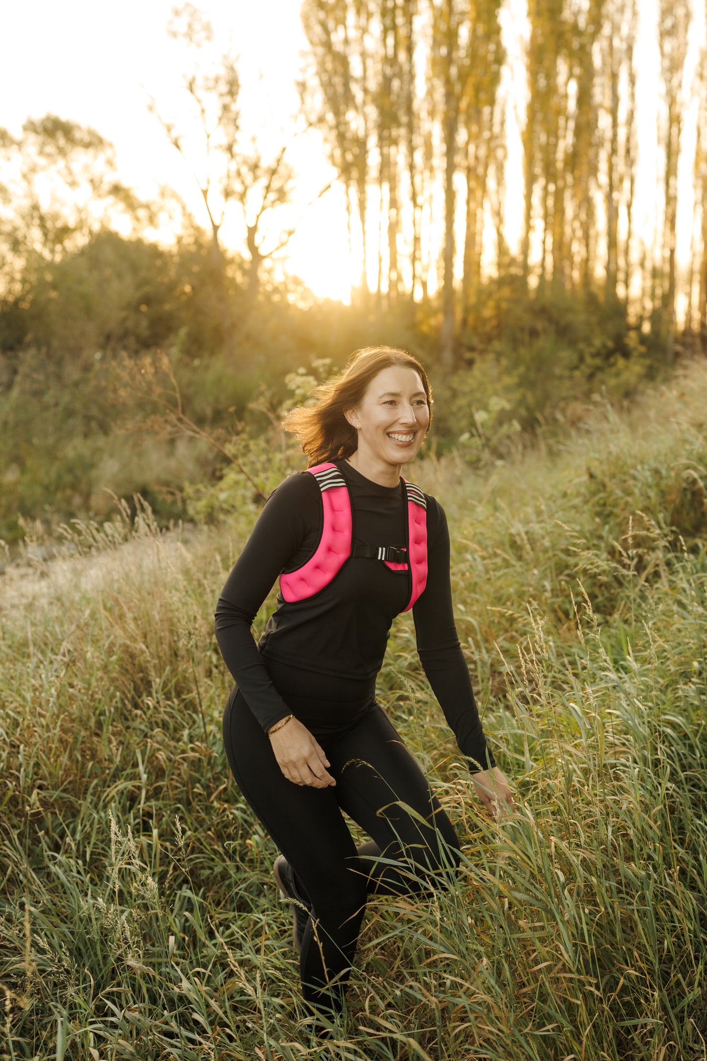 A lady exercising in the VestFit NZ pink weighted neoprene vest through forest grasses